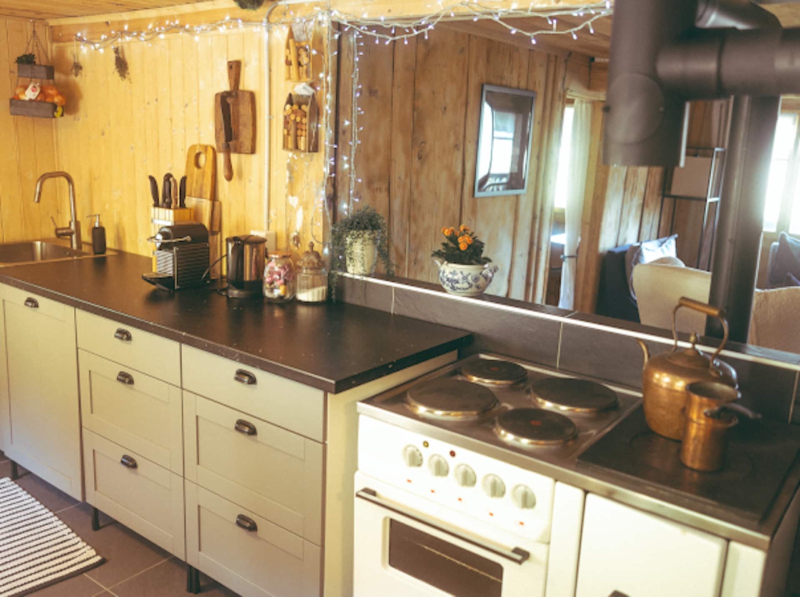 The chalet kitchen: cream cabinets, a dark stone counter, an oven and hob, a copper kettle, herbs and cutting boards against pine walls.