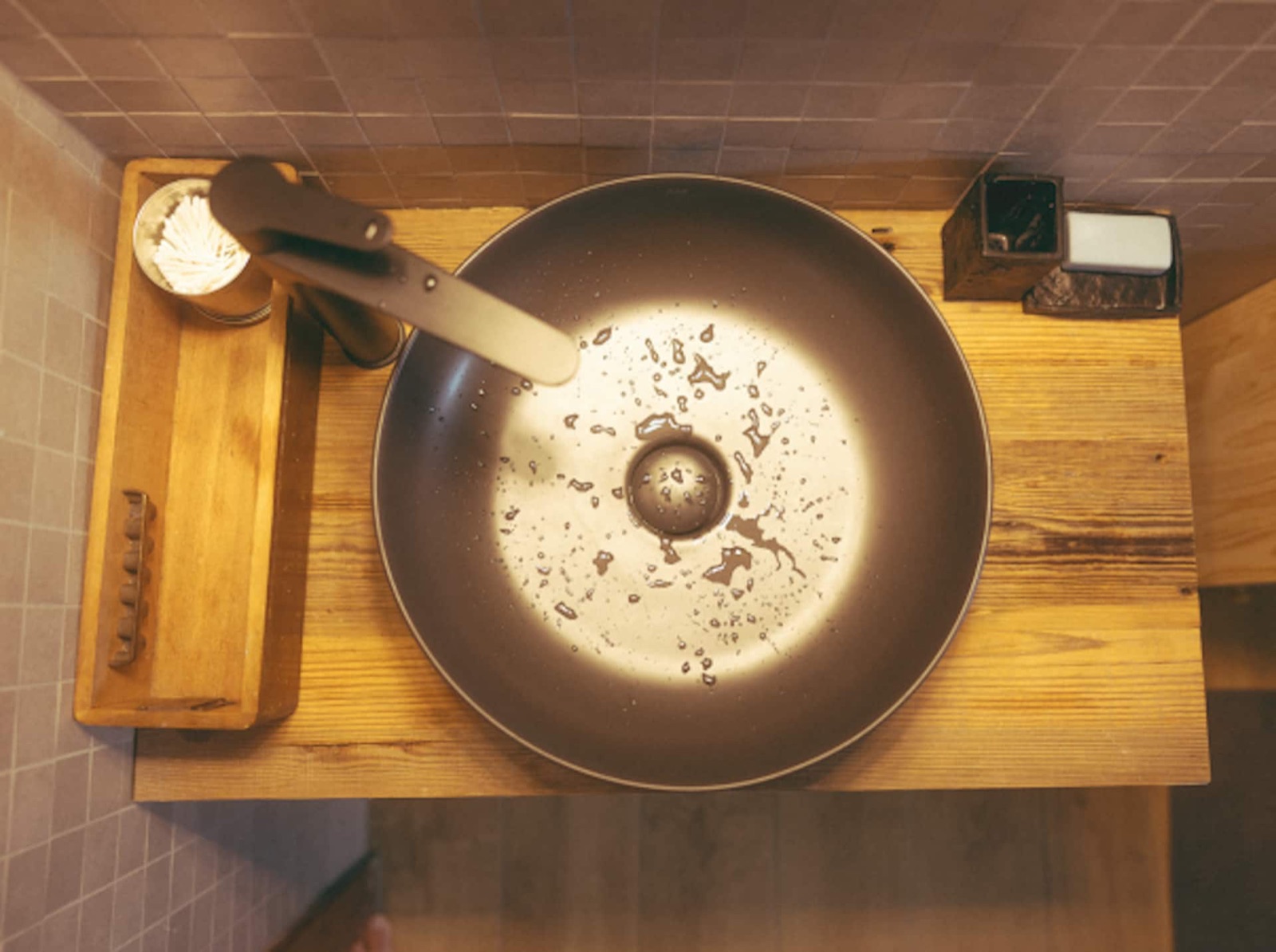 A round dark basin set on a solid wood counter with a wooden tray of essentials, seen from above.